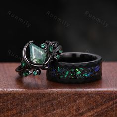 two rings with green and blue stones on them sitting on top of a wooden table