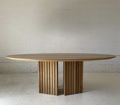 a round wooden table sitting on top of a white floor next to a brick wall