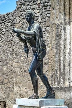 a statue of a man holding his arm out in front of a stone wall with an old building behind it