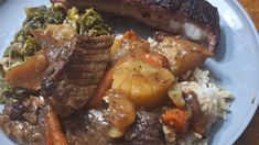 a white plate topped with meat, rice and veggies on top of a wooden table