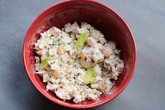 a red bowl filled with chicken salad on top of a gray countertop next to a fork