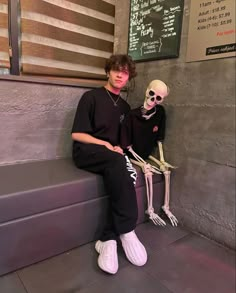 a boy sitting on a bench next to a skeleton