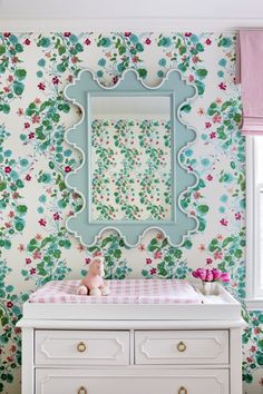 a baby's room with floral wallpaper and white dresser in the foreground