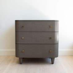 a gray dresser sitting on top of a hard wood floor next to a white wall