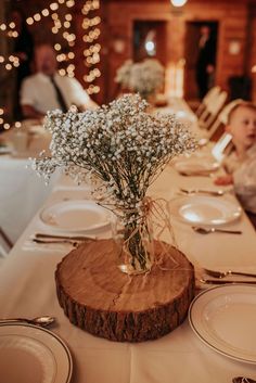 a vase with baby's breath sitting on top of a wooden slice at a table