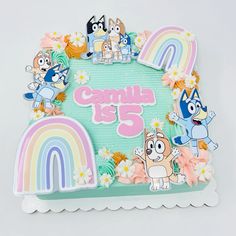 a cake with cartoon characters on it and rainbow in the background that says campila is 5