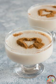 two glasses filled with pudding on top of a blue tablecloth and topped with cinnamon sprinkles