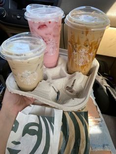 three starbucks drinks sitting on top of a tray in the back seat of a car