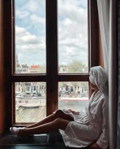 a woman is sitting on a window sill looking out at the water and buildings