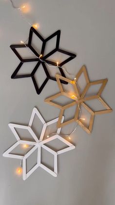 three wooden snowflakes with lights hanging from them on the wall in front of a white wall