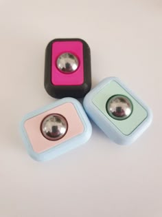 three square shaped objects sitting on top of a white table with one silver ball in the middle