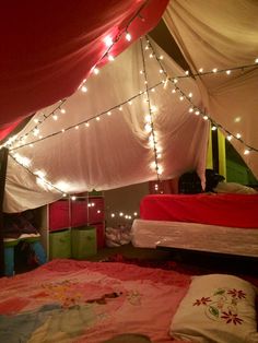 a bedroom with lights strung from the ceiling and bed sheets on the floor, in front of a tent