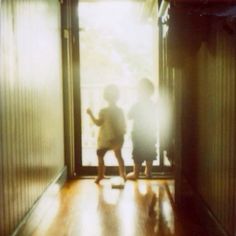 two children are standing in an open door with the light shining on them and one child is holding his hand out