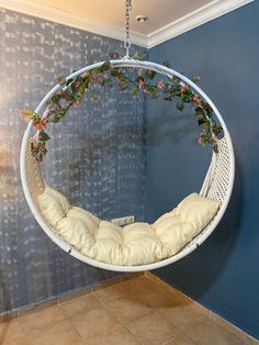 a white hanging chair with flowers on it in a room that has blue walls and tile flooring