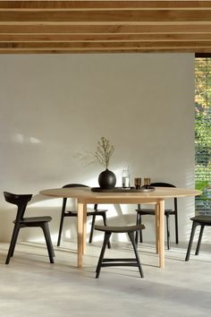 a dining table with chairs and a vase on it in front of a white wall