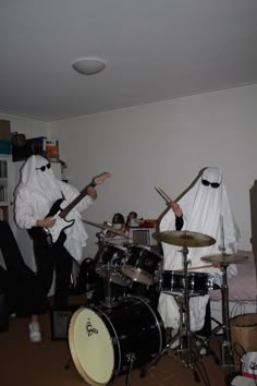 two people in white costumes playing drums and singing into microphones while another person dressed as ghost behind them plays guitar