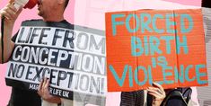 two people holding signs with words written on them and one person speaking into a microphone