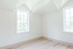 an empty room with two windows and hard wood flooring on the side, in front of white walls