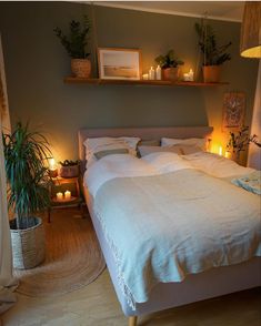 a bed with white linens and pillows in a bedroom next to two potted plants