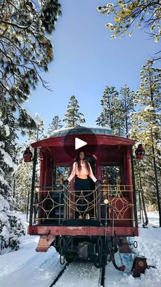 a woman standing on top of a red train car in the middle of snowy woods