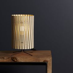 a wooden table with a lamp sitting on it's side and a black wall in the background