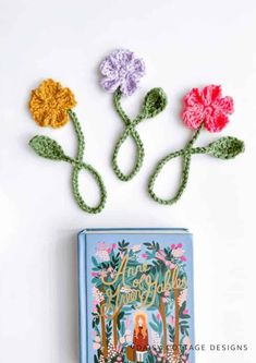 three crocheted flowers sitting on top of a blue box next to a book