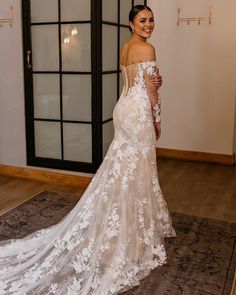 a woman in a white wedding dress standing on a rug with her back to the camera