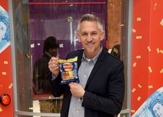 a man holding up a bag of chips in front of a red and white wall