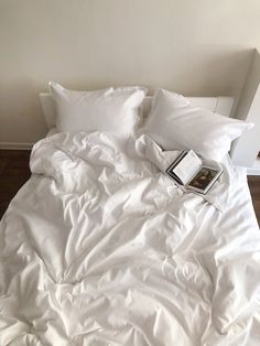 an unmade bed with white sheets, pillows and a book on the pillowcase