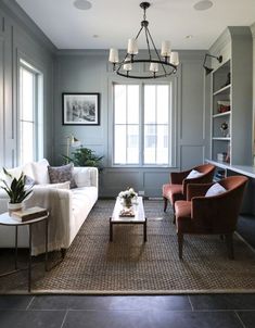 a living room filled with furniture and a chandelier hanging from the ceiling in front of two windows