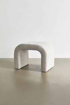 a small white bench sitting on top of a cement floor in front of a wall