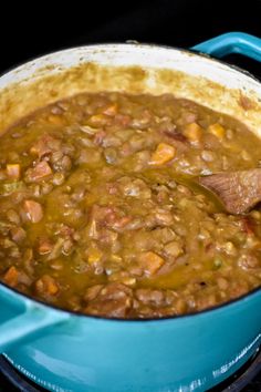 a blue pot filled with soup on top of a stovetop next to a wooden spoon