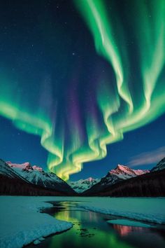 the aurora bore is seen above snow covered mountains and frozen water in this photo from alaska