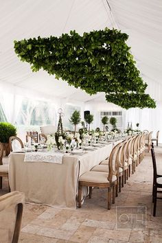 a long table with white linens and greenery hanging from it's ceiling