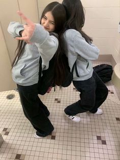 two girls standing in a bathroom pointing at the camera