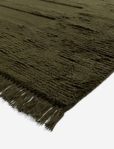 a dark green rug with fringes on the bottom and sides, in an angled view