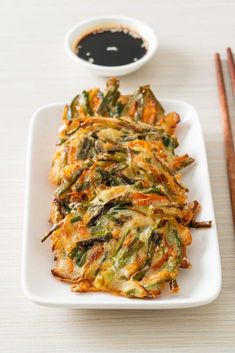 a white plate topped with fried vegetables next to chopsticks and sauce on a table