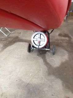 a red boat sitting on top of a cement floor next to a metal object with wheels