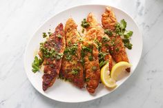 a white plate topped with fried fish and garnished with parsley next to a lemon wedge