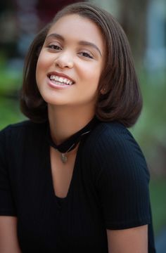 a young woman smiling and wearing a black shirt with her hair in a bobble