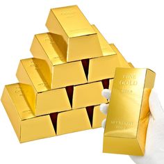 a hand holding a gold bar next to stacks of gold bars