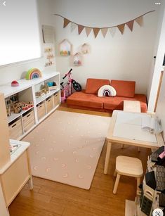 a small child's playroom with toys and furniture, including a couch, table, bookshelf, and toy storage bins