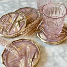 three pink glass coasters with gold rims on a marble countertop next to a cup and saucer