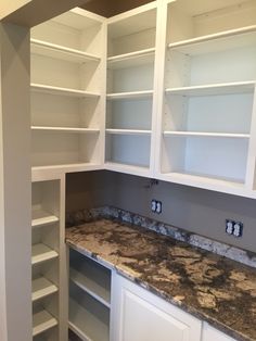 an empty kitchen with white cabinets and marble counter tops