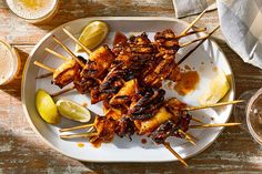 several skewers of food on a plate with lemon wedges and beer glasses