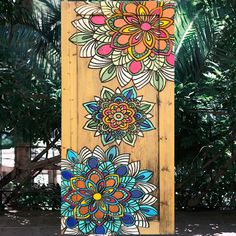 a wooden sign with colorful flowers painted on it's front and back sides, along with palm trees in the background