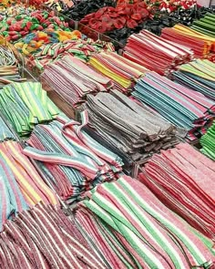 many different colored shirts are on display at a market stall with flowers in the background