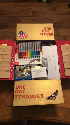 an open box with markers, pens and other items in it on a wooden table