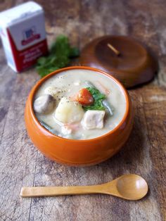 an orange bowl filled with soup next to a wooden spoon