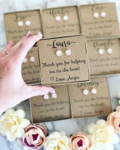 a person holding up some small earrings in front of several boxes with flowers on them